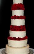 Candlelight buttercream iced,  6 tier round wedding cake decorated with white variegated patterned scrolls.Silver cake base.  (This cake can serve receptions with 300-455 expected guests)